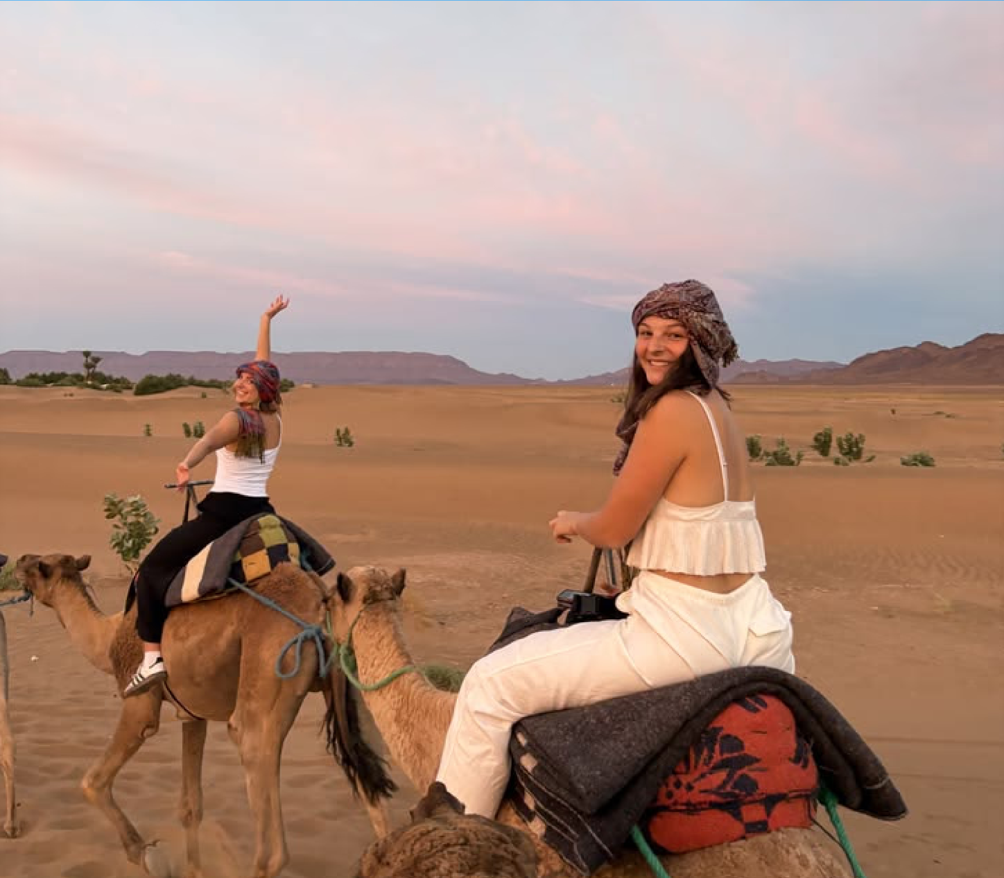 Guests smiling during a camel ride at dusk